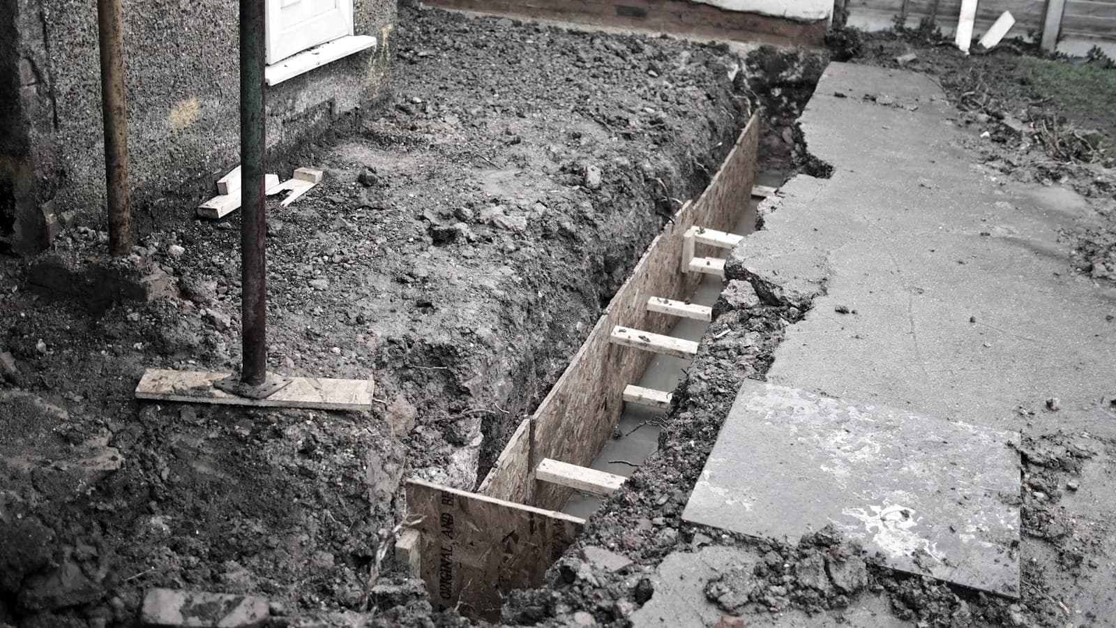 Excavated strip foundation trench alongside an existing house wall